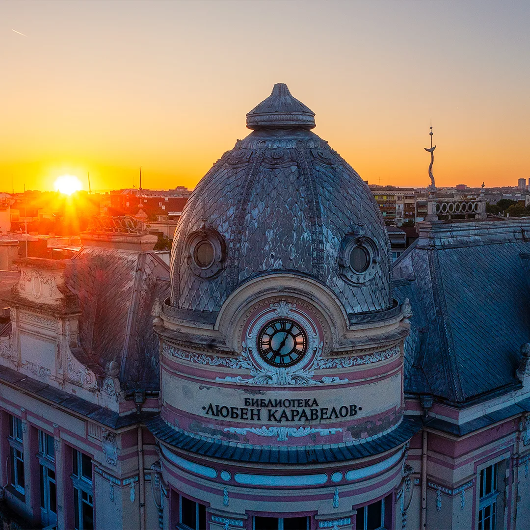 Close aerial view of the dome and clock of the Lyuben Karavelov Library in Ruse at sunrise, with the sun rising behind the building.