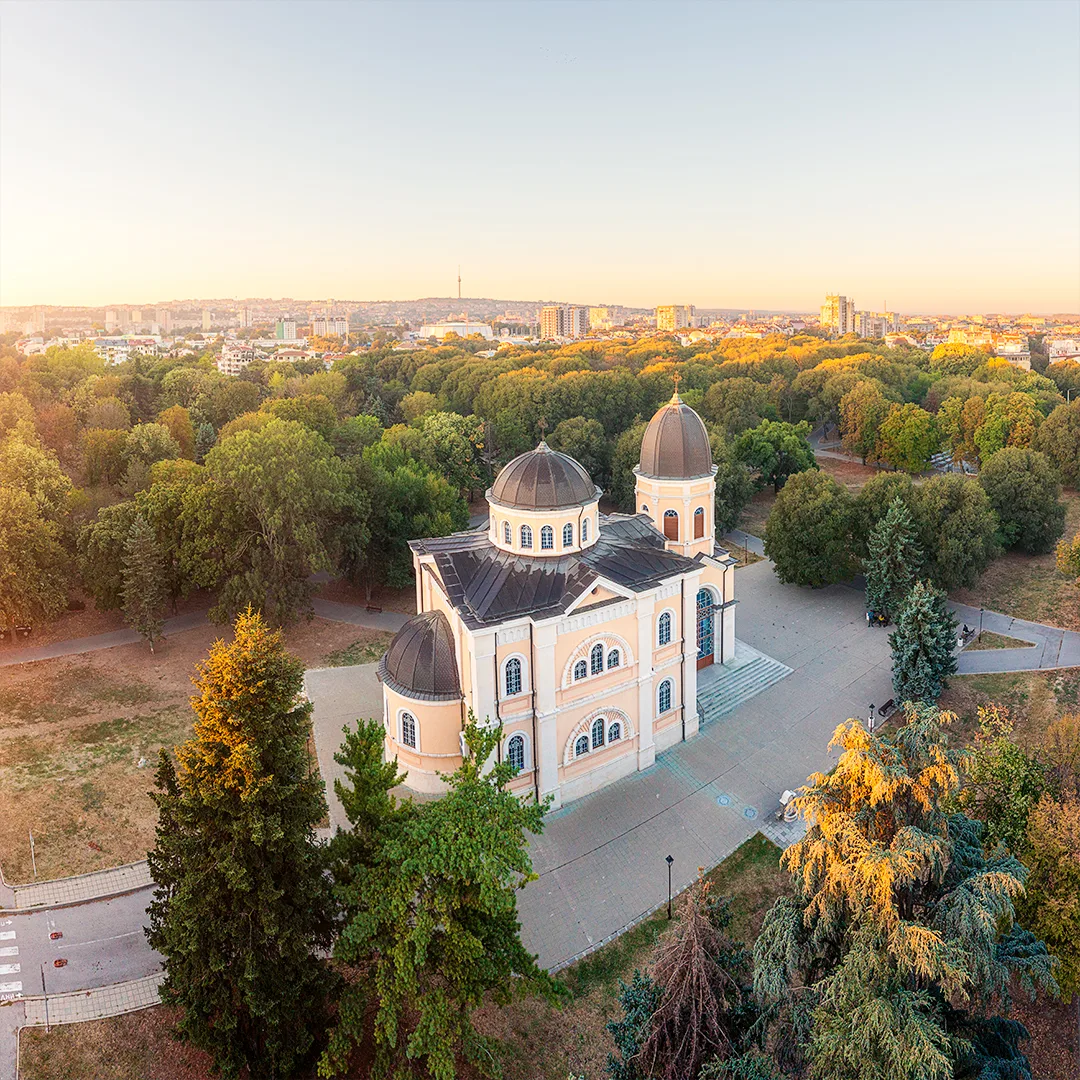 Aerial view of All Saints Church in Ruse surrounded by the trees of the Park of the National Revival Heroes in warm morning light.