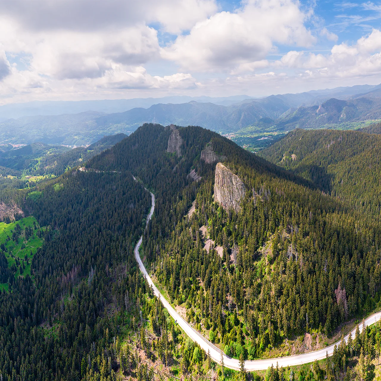 Aerial view of the Sokolitsa rock formation rising above a winding road and dense Rhodope forest.
