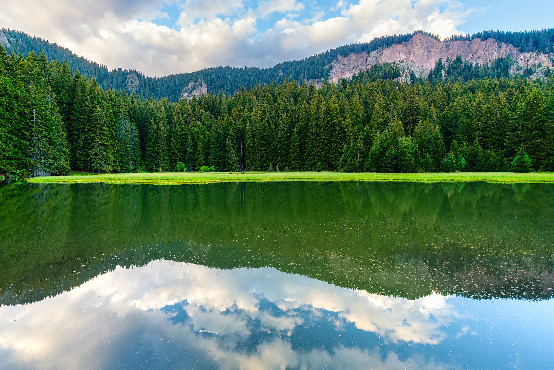 Calm Smolyan Lake reflecting clouds, coniferous forest and rocky cliffs in the Rhodopes.