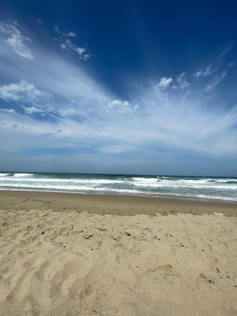 A wide sandy beach with rolling Black Sea waves beneath a blue sky filled with thin clouds.
