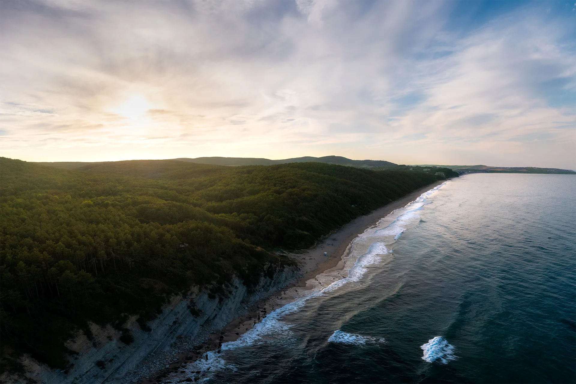 Aerial view of Chaika Beach, with a long sandy shoreline, dense forest and waves along the Black Sea coast.