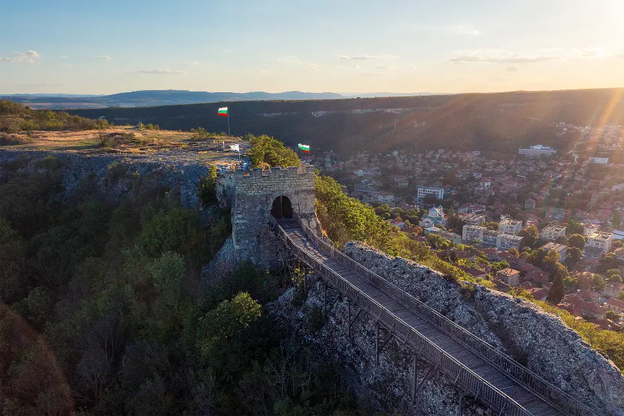 Ovech Fortress above Provadia at sunset, with the wooden bridge leading across the rocky plateau and the town stretching through the valley below.