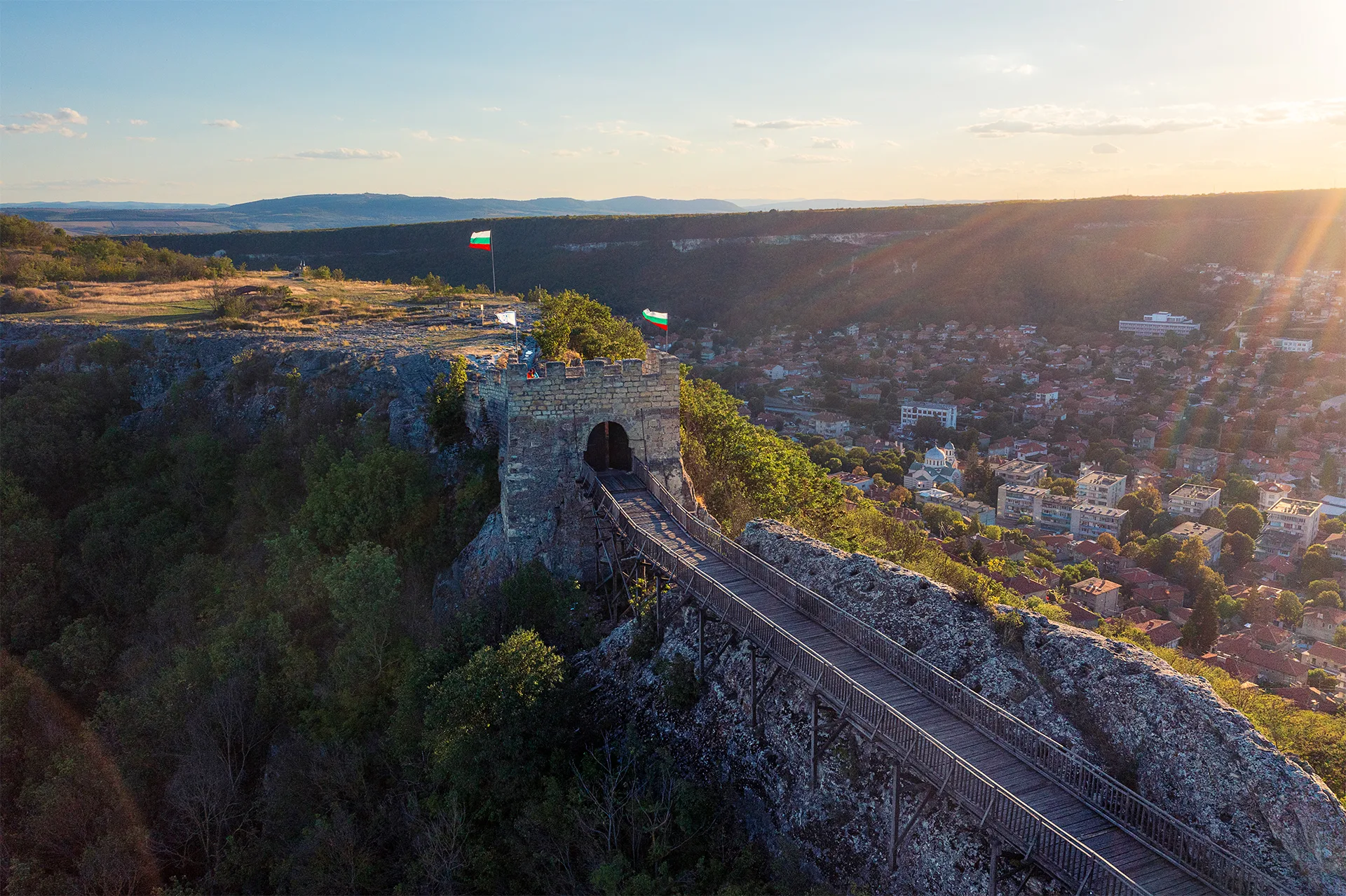Ovech Fortress above Provadia at sunset, with the wooden bridge leading across the rocky plateau and the town stretching through the valley below.