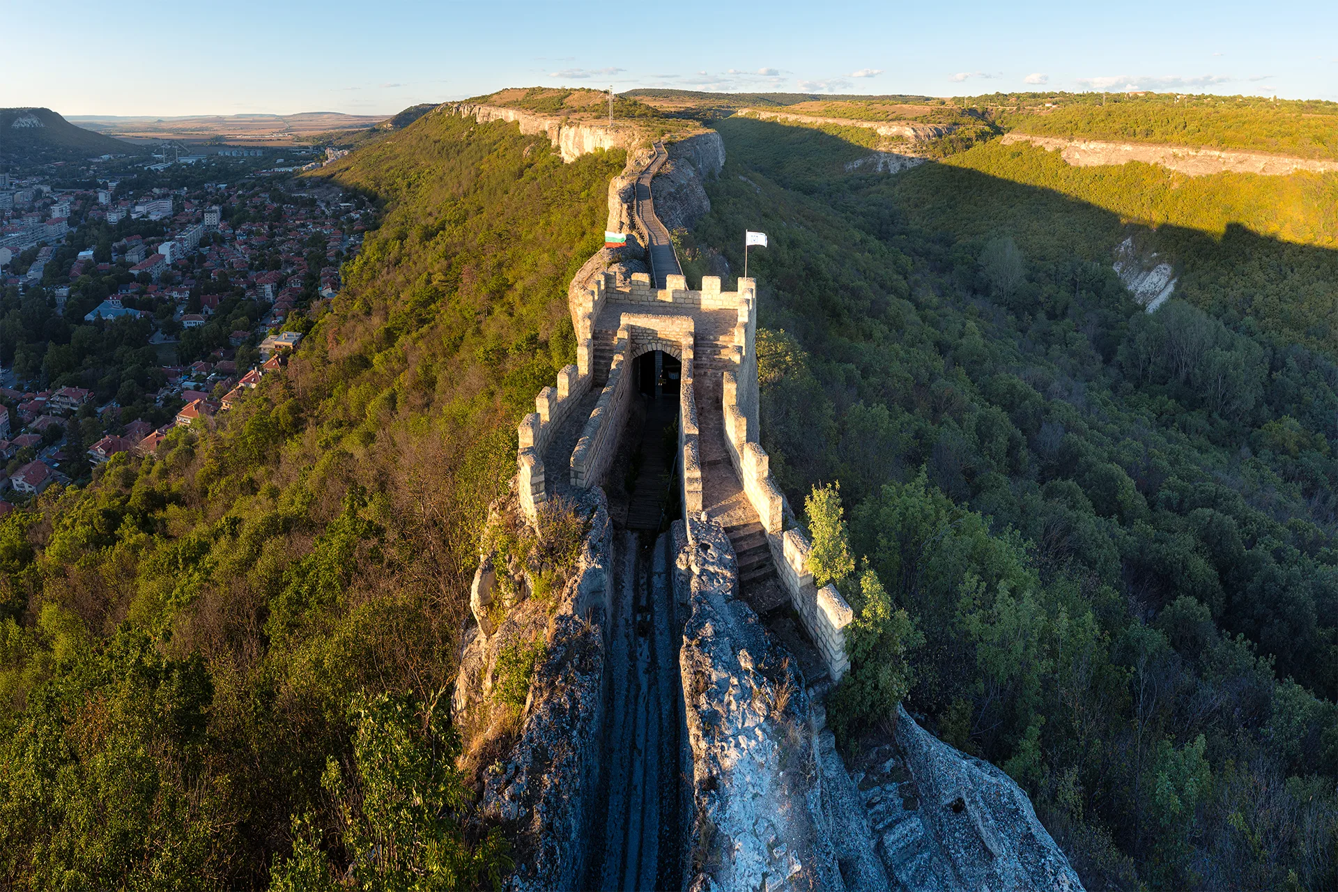 Aerial view of Ovech Fortress above Provadia, with the stone gate and narrow ridge leading across the plateau in warm evening light.