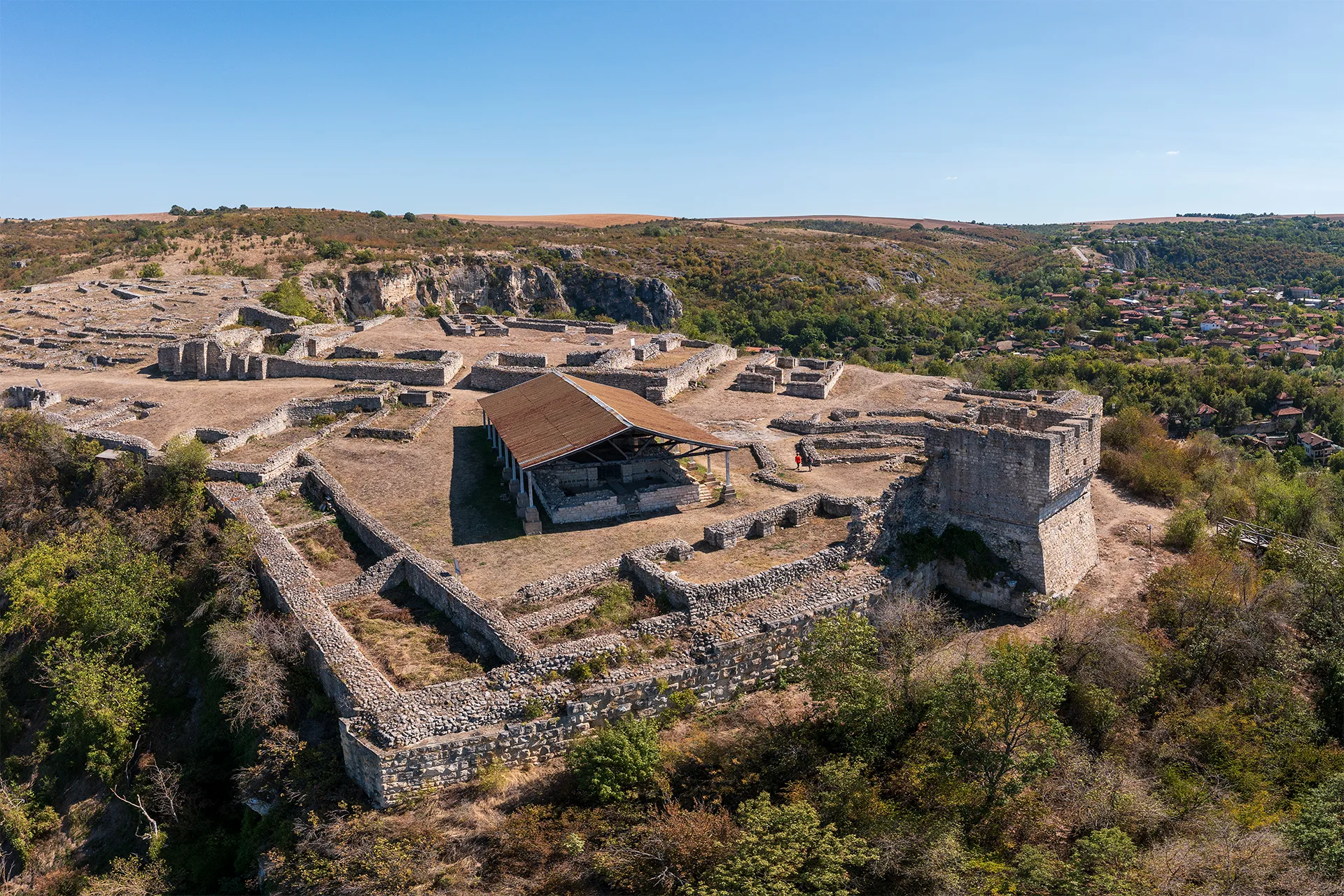 Aerial view of Cherven Fortress, with the remains of the medieval walls and buildings spread across the rocky plateau above the surrounding valley.