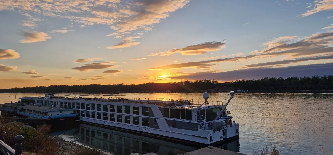 River cruise ship moored on the Danube in Ruse at sunset, with warm light reflecting across the water beneath scattered clouds.