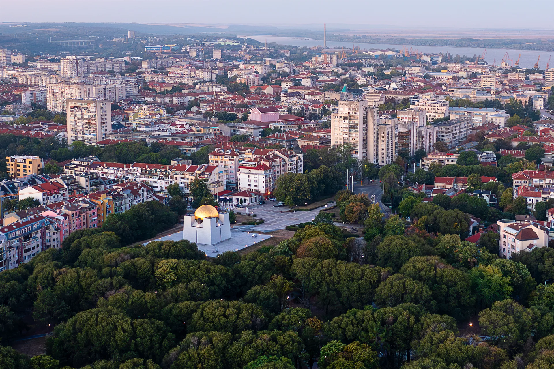 Aerial view of the Pantheon of National Revival Heroes in Ruse, surrounded by greenery, with the city and the Danube visible in the distance.