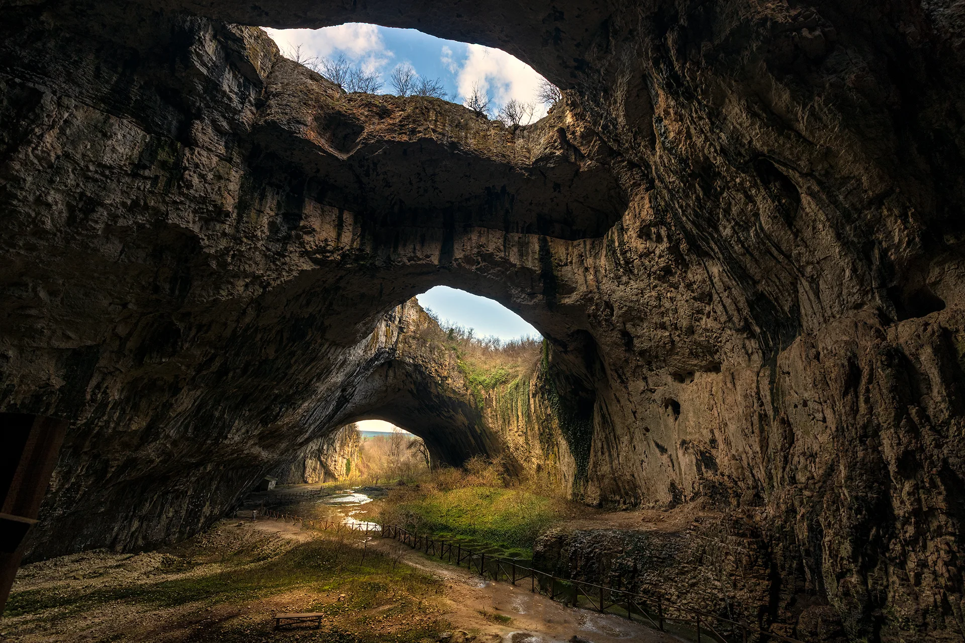 Interior of Devetashka Cave near Lovech, with massive rock arches, openings in the ceiling and natural light entering the cavern.