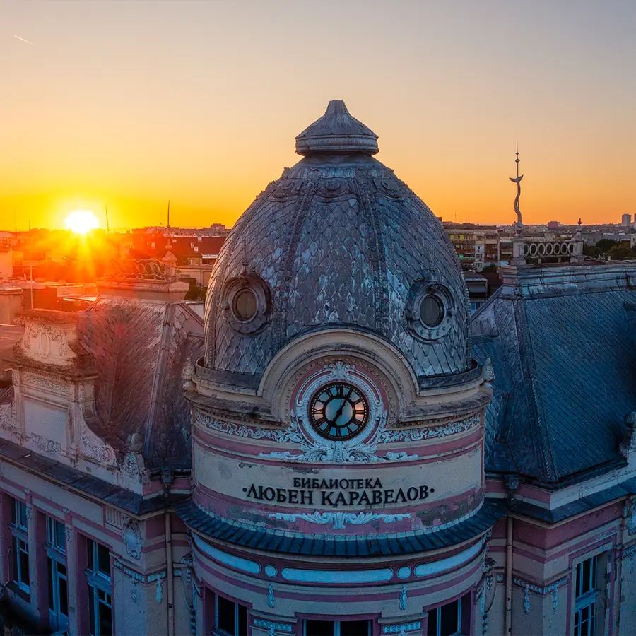 Close aerial view of the dome and clock of the Lyuben Karavelov Library in Ruse at sunrise, with the sun rising behind the building.