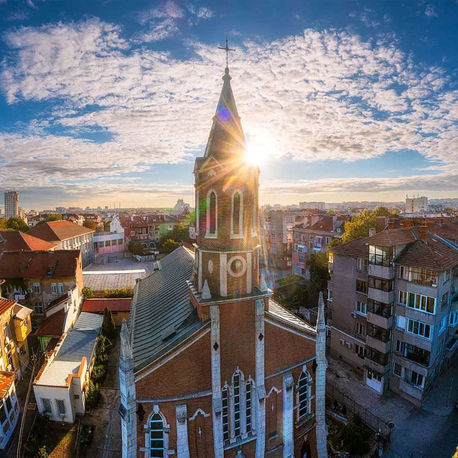 Aerial view of St Paul of the Cross Cathedral in Ruse with the rising sun shining behind its tall Gothic Revival bell tower.